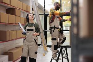Manager wearing headset working at products delivery, looking at shelves full with cardboard boxes. Storage room supervisor listening music while checking clients shipping details in warehouse photo