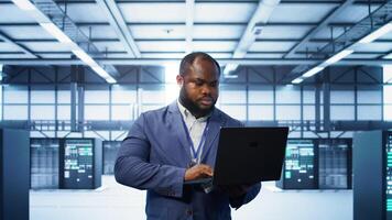Computer scientist in data center using diagnostic tools and system monitoring software on laptop to identify cause of errors. IT specialist in server farm establishment repairing equipment, camera B photo