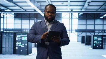 Software developer managing data center with advanced technology, ensuring efficient network management. Admin walking in server room, optimizing data center infrastructure with tablet, camera A photo