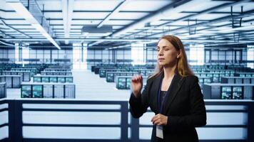 Software developer looking at holograms in data center, monitoring infrastructure. Woman in server room interacting with high tech augmented reality AI visualization, camera B photo