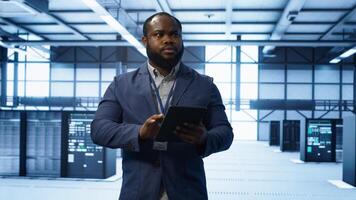 Software developer managing data center with advanced technology, ensuring efficient network management. Admin walking in server room, optimizing data center infrastructure with tablet, camera A photo