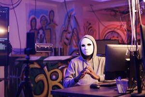 Anonymous criminal recording scam message on smartphone camera. Internet thief in mask with hidden identity broadcasting ransom on mobile phone to steal privacy information photo