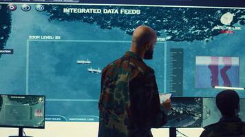 Army officer examining real time satellite data on big screen in military power base, gather intelligence on enemy vessels trajectory. Federal defense program specialist commanding troops. Camera B. photo