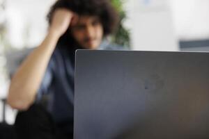 Start up company employee solving difficult business tasks and working on laptop in business office. Young arab project manager analyzing financial report statistics on computer photo