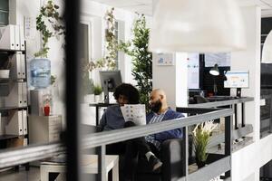 Two corporate employees discussing financial analysis and planning presentation in coworking space. Arab company analysts working in office, holding papers with charts and graphs photo
