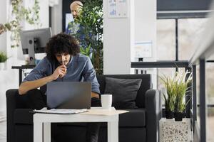Tired employee watching tutorial on laptop and taking notes to solve work task. Concentrated young arab executive manager analyzing product sales statistics on computer photo