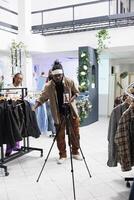 African american social media influencer promoting formal wear collection on smartphone camera in clothing store. Blogger showing jackets while filming live for followers in boutique photo