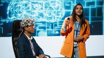 Speaker does EEG headset presentation during tech convention, demonstrating successful implementation of AI in driving forward startup businesses, sharing latest neuroscience discoveries, camera A photo