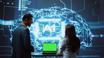 Startup coworkers brainstorming ways to use AI on chroma key notebook to improve data driven decisions. Technicians using mockup laptop to improve artificial intelligence tech, camera B photo