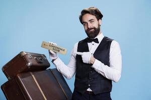 Skilled bellhop has conference room sign in hand, pointing at wall indicator to lead hotel guests to all locations on the premises. Stylish doorman posing with a pointer symbol. photo