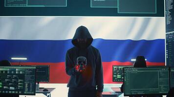 Conceptual image of a hooded russian hacker creating hazardous alerts, holds a skull and warning of death threats. Russian federation works on cybercrime and violence, panic and torment. Camera B. photo