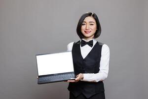 Smiling waitress presenting laptop with blank white screen for catering service software and looking at camera. Restaurant woman worker showing computer empty display portrait photo