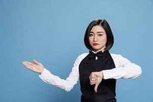 Waitress with thumb down showing negative feedback gesture and pointing to side portrait. Restaurant woman worker displaying disapproval symbol while showcasing to right with hand photo