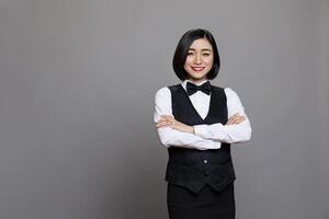 Smiling confident asian woman waitress in uniform standing with crossed arms portrait. Cheerful young professional receptionist posing with folded hands and looking at camera photo