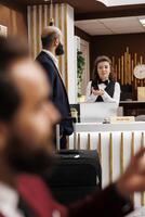 Receptionist greeting business traveller at front desk, sharing tips to ensure relaxing trip apart from meetings. Employee trying to help guest with accommodation, attention to details. photo