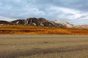 Majestic mountain chain in iceland, lonely road concept near fields and hills in nordic countryside. Beautiful roadside scenery and scandinavian landscapes, massive rocky cliffs with snow. photo
