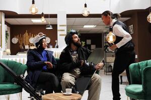 Excited couple with skiing and snowboarding gear receive assistance from friendly employee in hotel lobby. Visitors embrace winter adventure at ski resort ready for holiday activities. photo