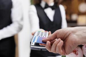 Close-up of an elderly caucasian man using his credit card to make a payment at the registration counter. Detailed view showing a person paying on pos terminal for reservation at hotel reception. photo