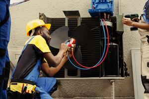 Proficient worker expertly refilling refrigerant in HVAC system while using barometer gauges to correctly measure the pressure in condenser, ensuring right cooling performance photo