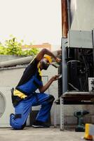 African american licensed serviceman hired for yearly condenser maintenance, using brush to remove debris from clogged air filter restricting airflow and decreasing efficiency photo