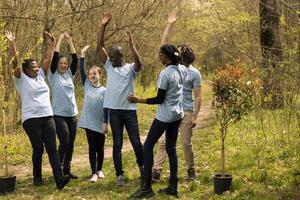 Team of diverse environmentalists linking hands to celebrate a successful mission of preserving natural habitat, saving the ecosystem. Group of people collaborate to grow more trees in the forest. photo