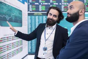 General director discussing with an investor to increase funding for a project, presenting performance metrics and annual data on a big screen. Business associates share strategies. photo