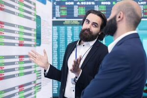 Members of the advisory board examines potential business expansion, supervisor look into data visualizations on a big screen in the office. Seeks to boost affordable earnings. photo