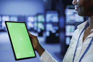 Trained technician in server room using mockup tablet to future proof network from downtimes and unexpected system failures. Expert with isolated screen device ensuring increased data security photo