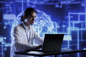 Asian admin in data center using artificial intelligence computing simulating human brain through self learning algorithms. Employee holding laptop, working with AI deep neural networks photo