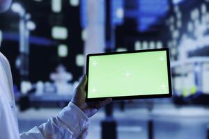 Man having fun walking around city at night, watching videos using mockup tablet, close up. Citizen using green screen device in landscape mode while strolling in empty metropolitan setting photo