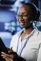 Pleased admin in data center uses tablet to prevent system hardware overload. Seasoned expert between server supercomputers ensuring enough network bandwidth for smooth operations photo