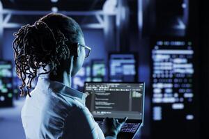 Computer scientist running code and programming on laptop, troubleshooting and upgrading high tech facility designed to accommodate multiple clusters of fully operational server rigs photo