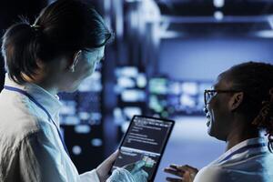 Engineer and african american colleague building firewall systems in server room. Man and woman running code on tablet to upgrade data center rigs handling demanding workloads photo