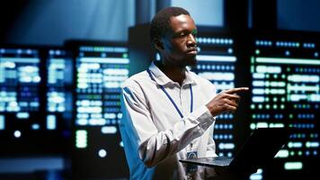 African american meticulous employee walking through server rows providing vast computing resources and storage, enabling artificial intelligence to process massive datasets for training and inference photo