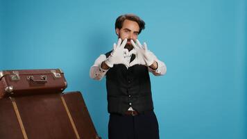 Smiling bellhop does heart shape sign in studio, indicating romantic emotions and flirting on camera while he wears suit and tie. Sweet doorkeeper showing romance gesture for love, sincere feelings. photo