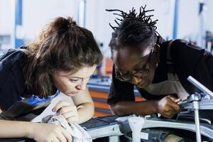 African american mechanics collaborating on servicing broken vehicle, checking for faulty radiator. Multiethnic women in auto repair shop working together on fixing car, discussing best options photo