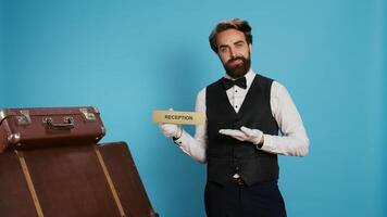 Hotel staff shows reception pointer on camera, leading guests in the right direction or area. Professional luxury doorman working in tourism travelling sector, showing front desk indicator. photo