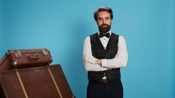 Confident bellboy posing on camera, wearing formal attire while he works at luxurious hotel. Staff member standing next to pile of suitcases and trolley bags, provide excellent concierge service. photo