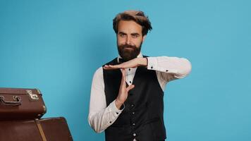Hotel worker indicates timeout sign in studio, asking for work break and presenting hospitality and travel sector. Stylish doorkeeper in formal clothes showcasing pause symbol with hands. photo