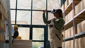 African american employee in warehouse wearing VR headset, using technology to visualize how to best stack cardboard boxes on shelves to make room for more. Worker in storage room uses virtual reality photo