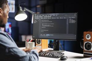 IT specialist writing html script binary code for database security, working on server optimization at home. African american hardware expert works on software programming, technical support. photo