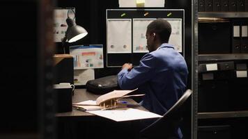 africano americano privado detective clausura y embalaje su computadora portátil, dejando el oficina habitación. negro policía ajuste arriba su puesto de trabajo, arreglando archivos y que lleva su ordenador portátil bolsa. foto