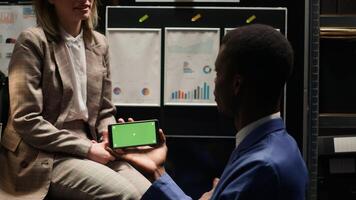 Private investigator looking at isolated copyspace display while horizontally holding smartphone with greenscreen. In evidence room, policeman utilising chromakey mockup template on mobile device. photo