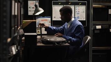 africano americano investigador llega oficina en adornado con crimen escena fotos y marcado mapas, que lleva ordenador portátil bolsa. colocación ordenador portátil en mesa, detective meticulosamente comentarios evidencia archivos.