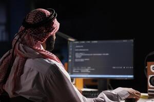 Arab software developer typing code and focused on running algorithms, showcasing his programming skills. Computer screen displays a user interface, highlighting the importance of internet security. photo