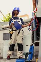 Adept repairman commissioned to optimize HVAC system efficacy, ensuring it operates at maximum capability. Proficient worker doing condenser unit investigation, imputing data on laptop photo