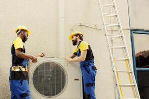 African american mechanic and apprentice repairman taking apart old damaged external hvac system to replace it with new performant air conditioner after draining refrigerant and replacing ductwork photo