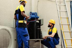 Servicemen fixing damaged blower fan causing frozen evaporator coil, resulting in reduced cooling performance. Seasoned wiremen optimizing HVAC system, ensuring it operates at maximum power photo