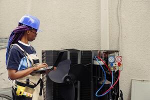 Qualified electrician commissioned to optimize HVAC system efficacy, ensuring it operates at maximum ability. Licensed efficient electrician doing air conditioner survey, imputing data on laptop photo