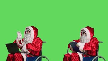 Papa Noel en videollamada con portapapeles archivos, relación comercial con crónico invalidez en silla de ruedas terminado pantalla verde. padre Navidad utilizando en línea conferencia charla y tomando notas en documentos, fiesta concepto. foto